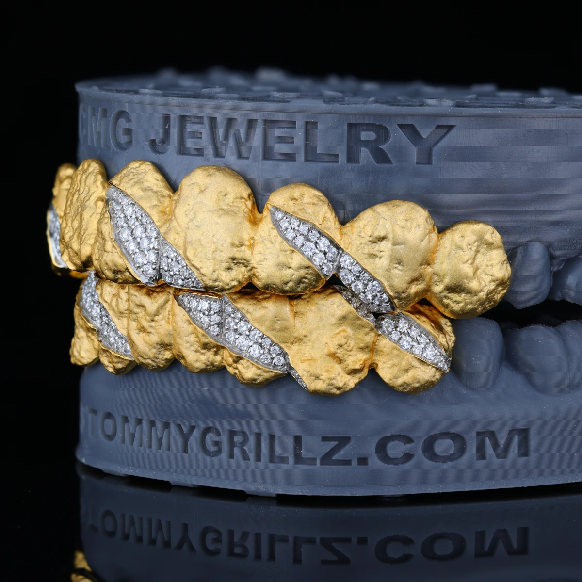 Textured gold-tone grillz with claw-shaped clear stone accents on a dental model.
