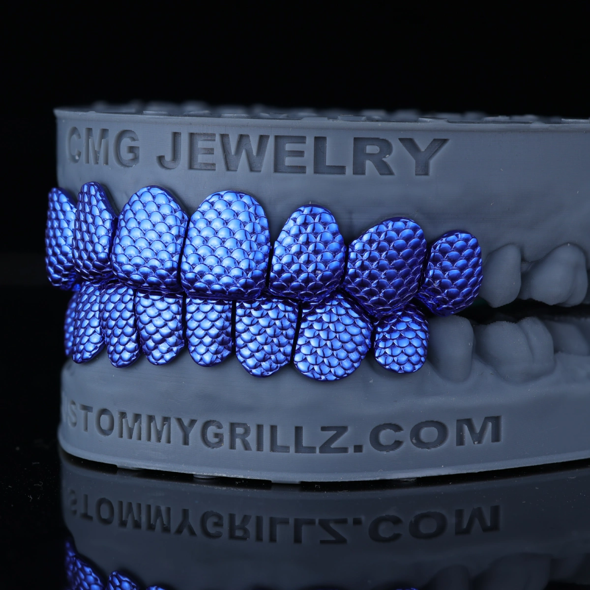 Blue scale-pattern upper and lower grillz on a gray dental model against a black background.