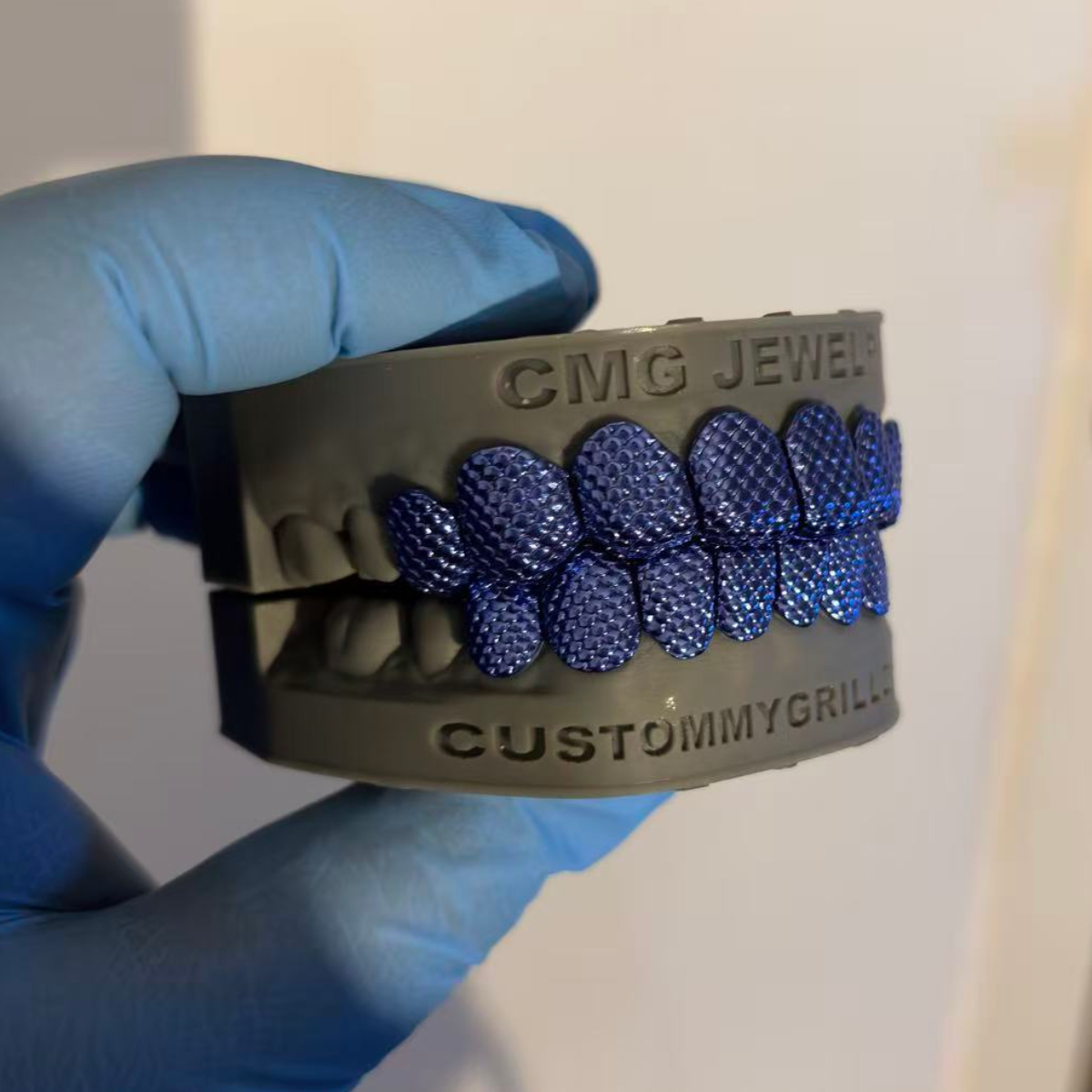 Blue scale-pattern upper and lower grillz displayed on a dental model held in a gloved hand.