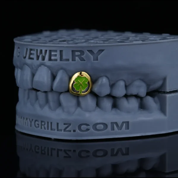 Single-tooth gold-tone grillz with a green clover enamel design.
